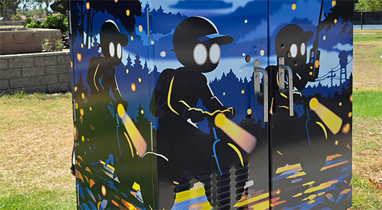 Utility box wrap of night scene with full moon and stars, with three dark figures with glowing eyes, each riding a bike. 